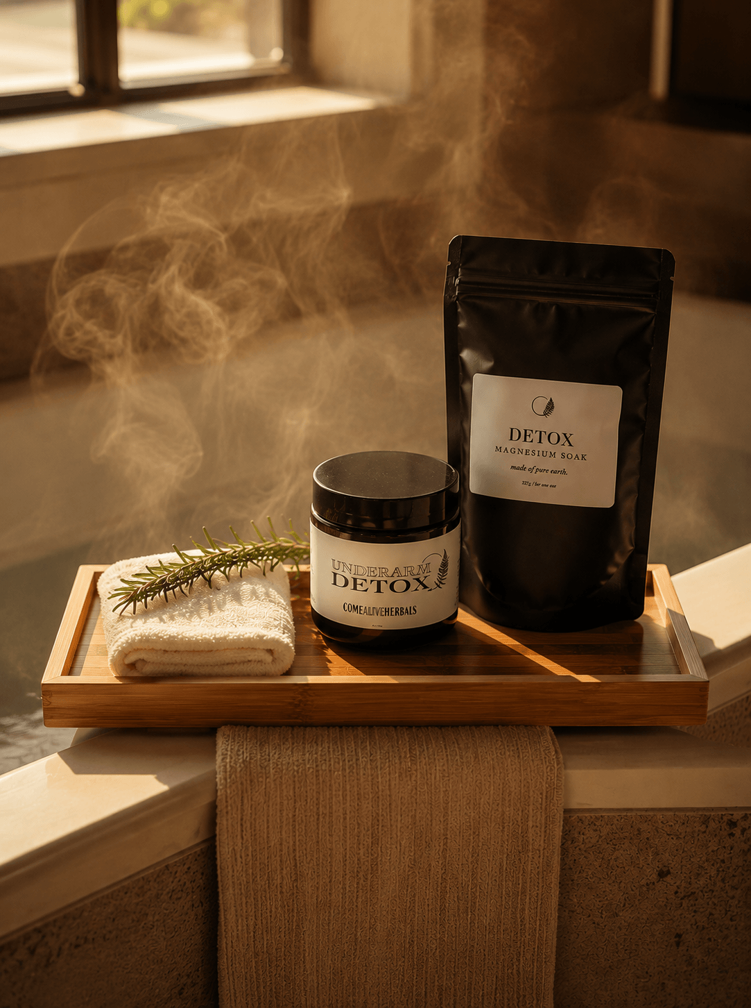 A spa-style detox product set displayed on a wooden tray in a warm, steam-filled bathroom setting. The set includes a black stand-up pouch labeled 'DETOX MELANINIC PINK', a matching black jar labeled 'DETOX', a folded white towel, and a sprig of greenery.