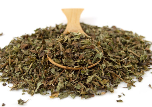 Dried green Organic Lemon Balm herbs with a wooden spoon on a white background.
