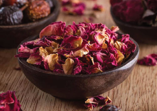 Dark wooden Bowl of dried pink and yellow Rose petals on a wooden surface