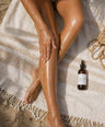 Person with sun-kissed legs on a towel next to a bottle of SOLUDE skincare product.