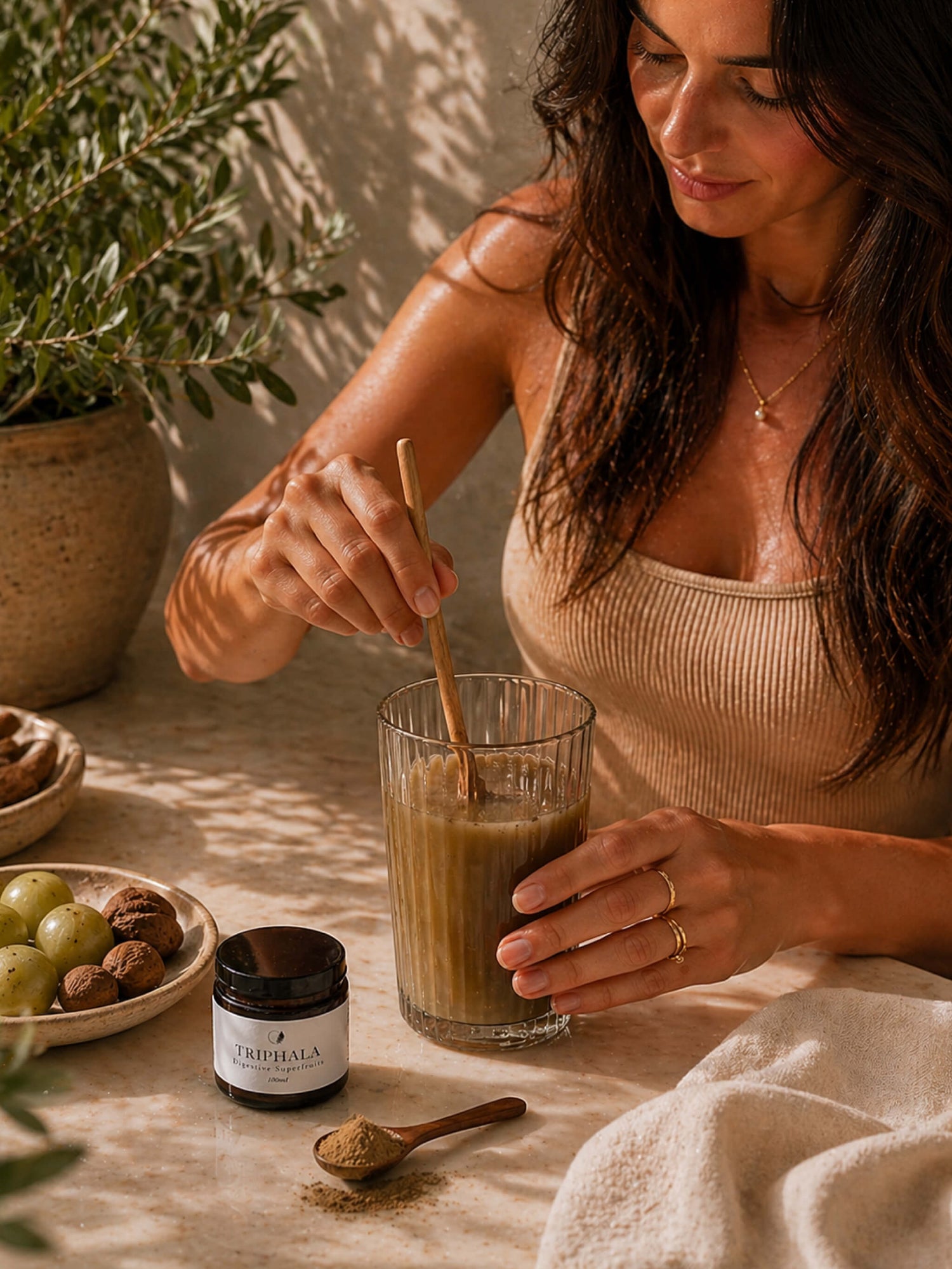 Woman stirring a drink in a glass with a wooden spoon, surrounded by natural elements.